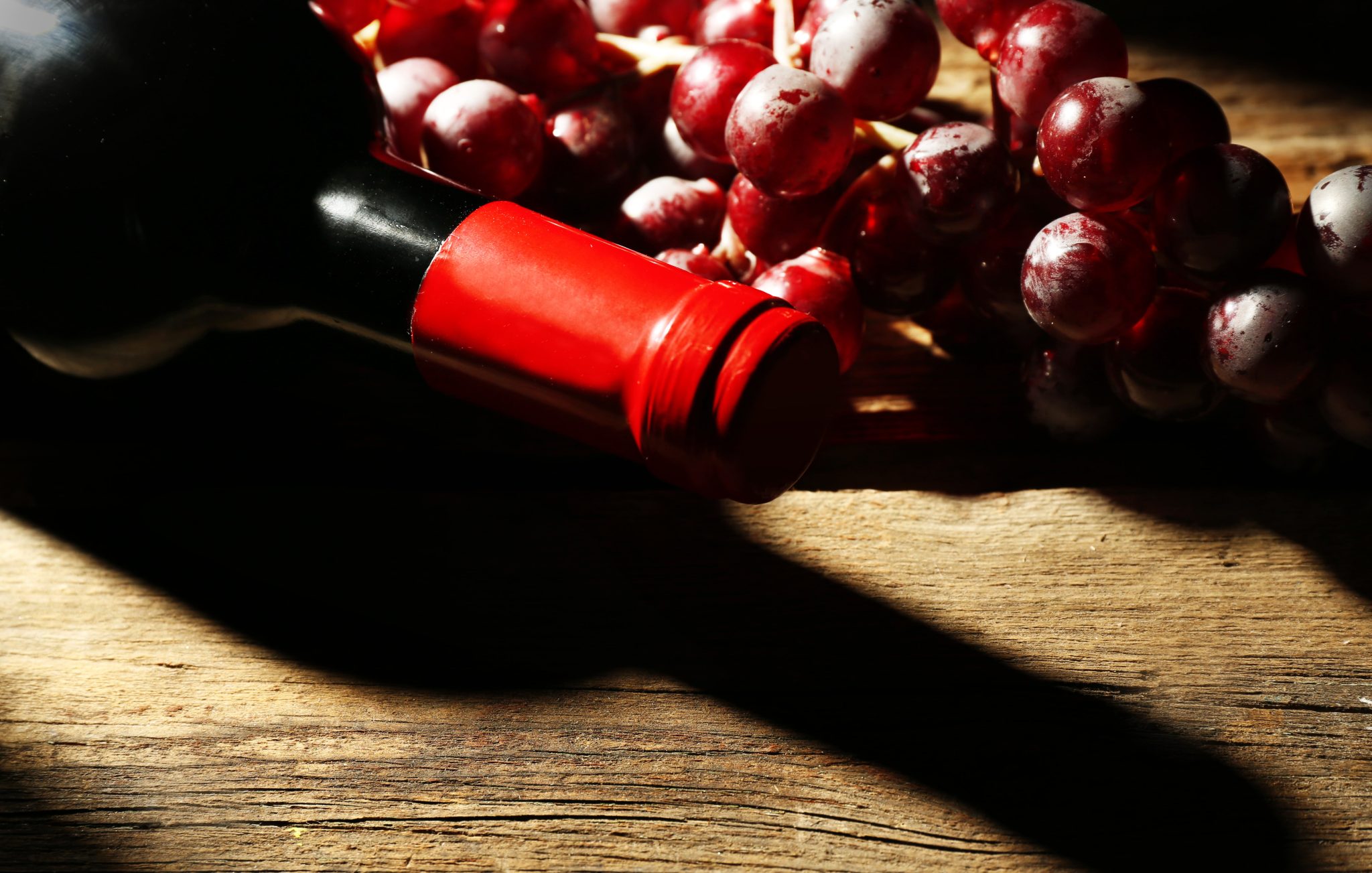 bouteille en verre de vin avec bouchons et raisins dans l obscurite avec lumiere sur fond de table en bois min